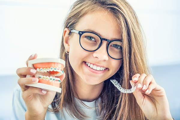 Invisalign vs braces - girl holding braces and an Invisalign tray