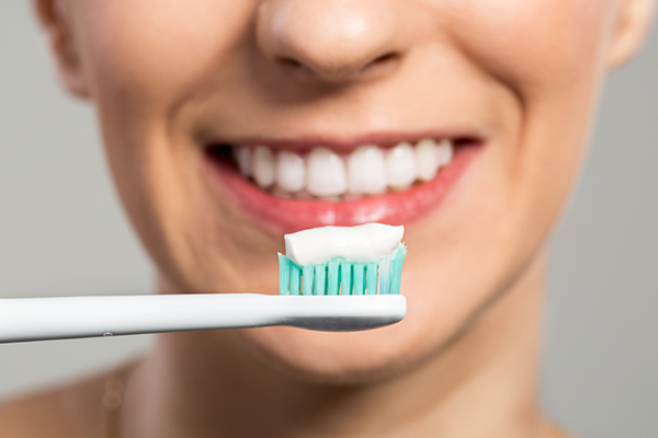 smiling woman holding a toothbrush with whitening toothpaste
