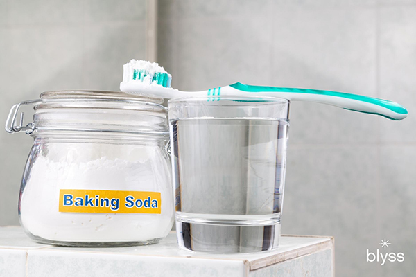 toothbrush placed on top of the glass with water beside a jar of baking soda